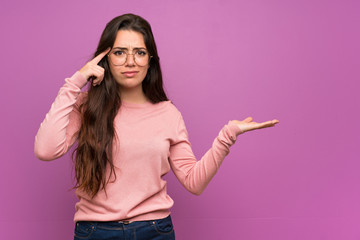 Teenager girl over purple wall making the gesture of madness putting finger on the head