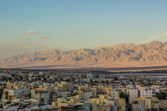 Muslim modern small city view in Middle East desert scenic landscape and sand stone mountain ridge out into the distance background in evening sunset soft orange lighting 