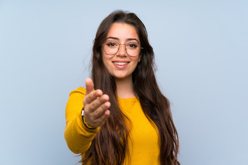 Teenager girl over isolated blue wall handshaking after good deal