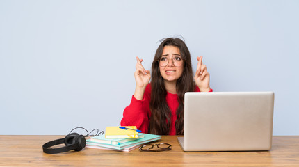 Teenager student girl studying in a table with fingers crossing and wishing the best