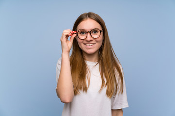 Young woman over blue wall with glasses and surprised