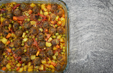 on marble floor, meatballs with vegetables, in glass baking dish