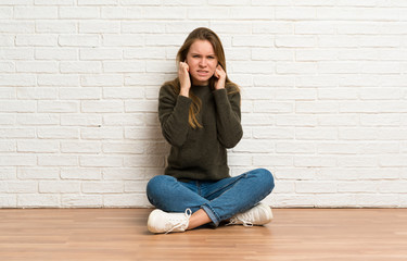 Fototapeta na wymiar Young woman sitting on the floor frustrated and covering ears
