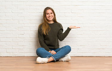 Young woman sitting on the floor holding copyspace imaginary on the palm to insert an ad