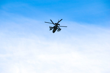 Russian military combat attack helicopter K-52 Alligator flies against a blue sky and clouds