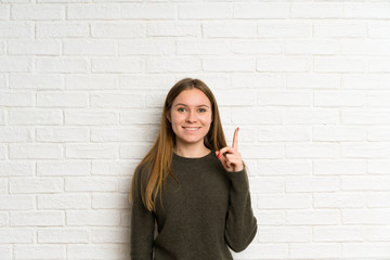 Young woman over white brick wall pointing with the index finger a great idea