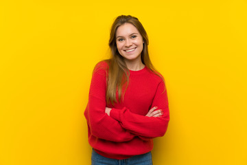 Young woman over yellow wall keeping the arms crossed in frontal position