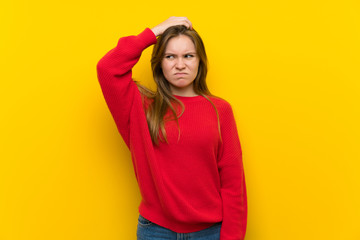 Young woman over yellow wall having doubts while scratching head
