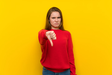 Young woman over yellow wall showing thumb down with negative expression