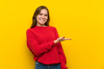 Young woman over yellow wall presenting an idea while looking smiling towards