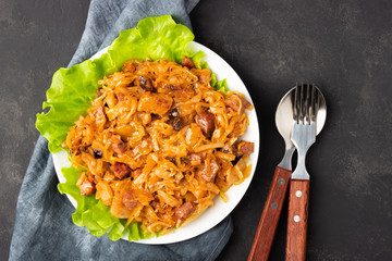 Traditional dish of polish cuisine - Bigos from fresh cabbage, meat and prunes. Top view. Dark background.