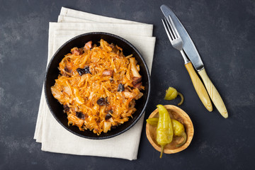 Traditional dish of polish cuisine - Bigos from fresh cabbage, meat and prunes. Top view. Dark background.