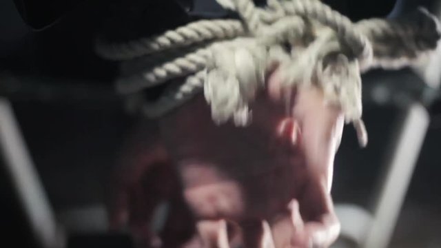 Close up of human hands tied with white colored rope and sitting on a metal chair.