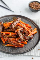 Close-up of Chinese spicy Szechuan beef meal on a black plate with wooden sticks over white table. Asian food recipe, portion for one person.