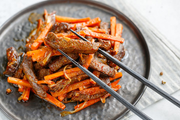Close-up of Chinese spicy Szechuan beef meal on a black plate with wooden sticks over white table. Asian food recipe, portion for one person.