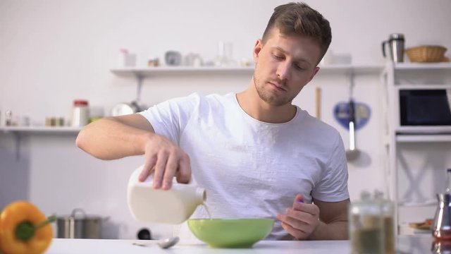 Handsome male eating corn flakes with milk, nourishing and healthy breakfast