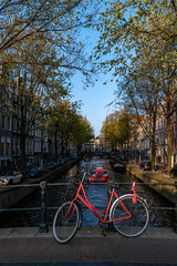 Fototapeta na wymiar Red bicycle parking on the bridge over the calm water of a canal with a boat giving a round trip to tourists, Amsterdam, Netherlands
