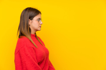 Young woman over isolated yellow wall keeping arms crossed and looking side