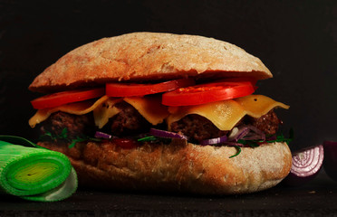 Closeup of delicious fresh homemade burger with lettuce, cheese, onions and tomatoes on dark background
