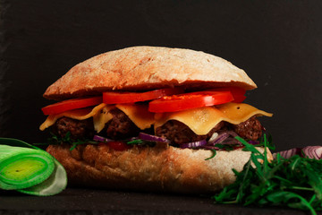 Closeup of delicious fresh homemade burger with lettuce, cheese, onions and tomatoes on dark background
