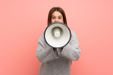 Young woman over pink wall shouting through a megaphone