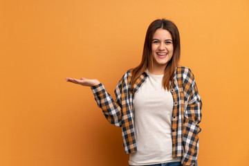Young woman over brown wall holding copyspace imaginary on the palm to insert an ad