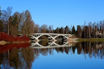 An old grey bridge over a calm river. Clear blue sky is reflecting on a springlike water surface