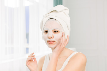 Closeup portrait of young pretty woman applying paper sheet mask on her face. Cosmetic procedure. Beauty spa and cosmetology.