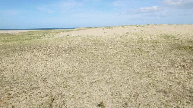 Low altitude forward aerial drone video hugging sand dune terrain of empty beach ascending to reveal the Mediterranean Sea