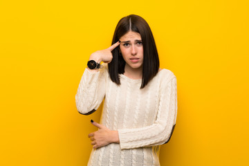 Young woman over isolated yellow wall making the gesture of madness putting finger on the head