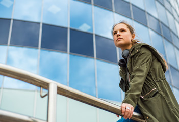 Outdoo portrait of young teenager brunette girl with long hair. Glass building on background with copy space.