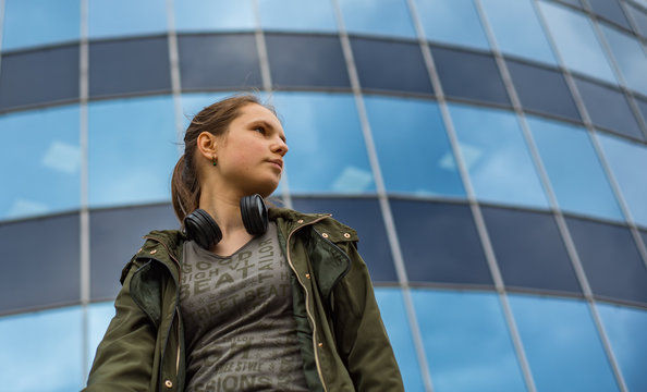 Outdoo portrait of young teenager brunette girl with long hair. Glass building on background with copy space.