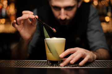 Bartender pours cocktail with red berry using forceps