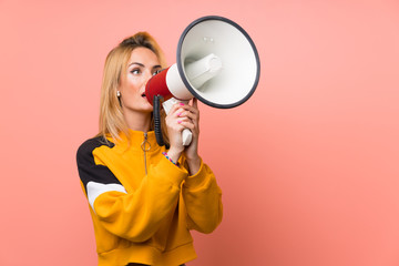 Young blonde woman over isolated pink background shouting through a megaphone