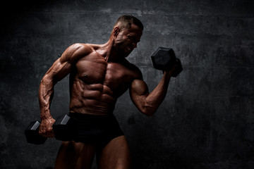 Fototapeta premium Muscular Men Exercise With Weights. He is performing biceps curls with dumbbels and barbell