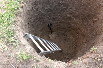 Deep pit in the ground. In the pit shovel and ladder. Digging a hole.