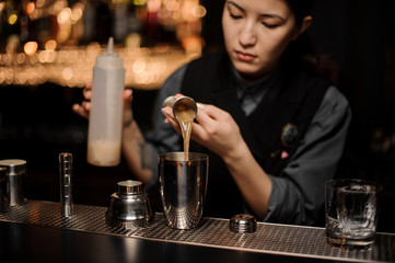 Female bartender preparing cocktail with sour mix in shaker