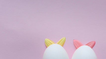 two Easter white eggs with rabbit ears made of gerbera petals on grey background