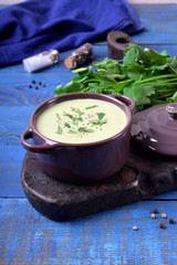 Green cream soup in a ceramic pan against the blue background