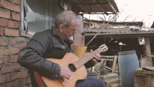 an elderly man playing guitar in his yard in the village, a happy man enjoys life