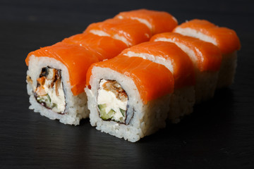 Philadelphia roll sushi with salmon, avocado, cream cheese served on black stone slate