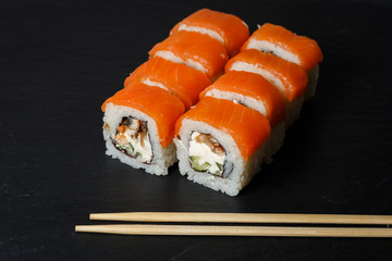 Philadelphia roll sushi with salmon, avocado, cream cheese served on black stone slate
