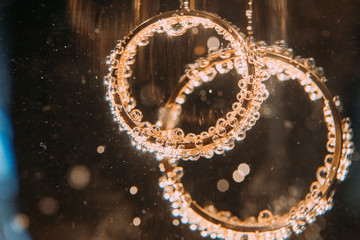 Wedding golden rings in glass of champagne. Symbol of love and marriage. Creative picture with champagne bubbles, glittering in the sunlight