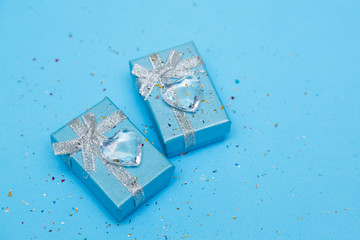 Blue gift box with jewelry and crystal heart, around sequins. Blue background.