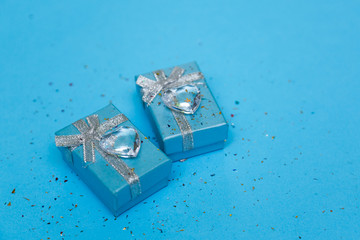 Blue gift box with jewelry and crystal heart, around sequins. Blue background.