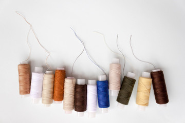 Row of number of different colors colorful multicolored sewing thread spools on light blue...