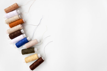 Row of number of different colors colorful multicolored sewing thread spools on light blue background. Selective soft focus, text copy space.