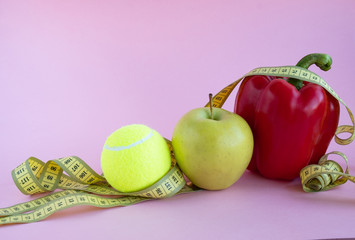 A red pepper, a tennis ball and a green apple are wrapped in a measuring tape. concept of sports and healthy eating