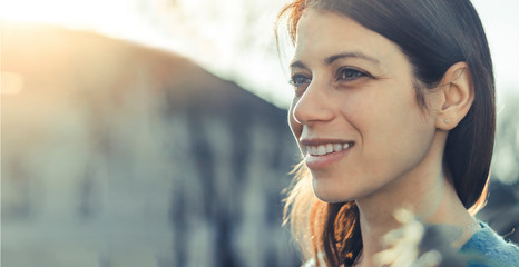 Closeup of a smiling young woman looking into the distance at sunset. - Powered by Adobe