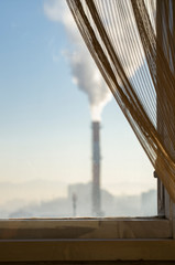 Factory chimney tower producing toxic white smoke seen through window